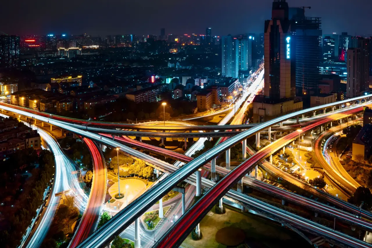 A city highway interchange at night, freight corridors lit by light trails