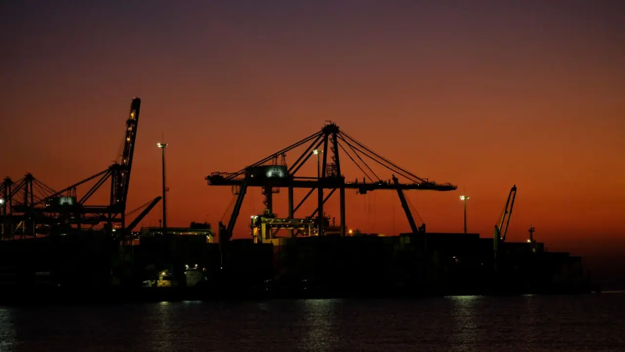 Container cranes silhouetted against a dusk sky at a cargo port