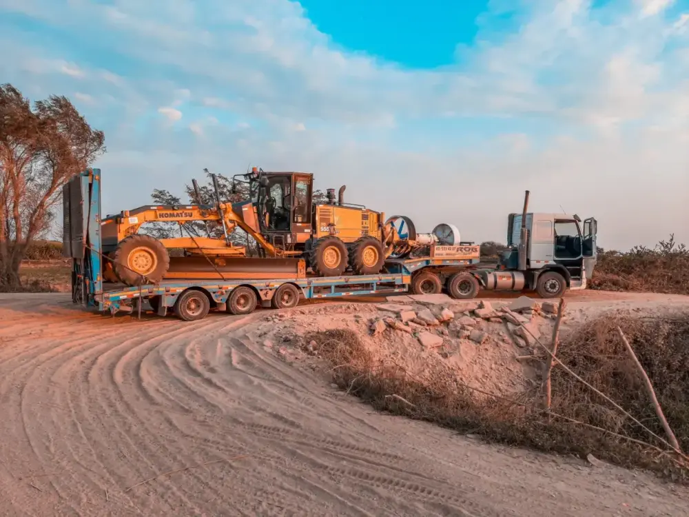 A low-loader truck transporting heavy machinery on a rural road